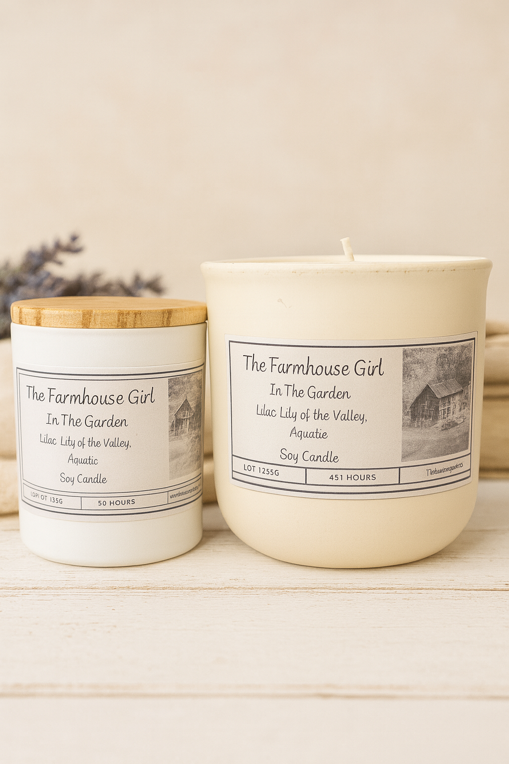 Two candles from 'The Farmhouse Girl' on a wooden surface with a neutral background.