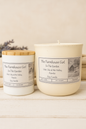 Two candles from 'The Farmhouse Girl' on a wooden surface with a neutral background.
