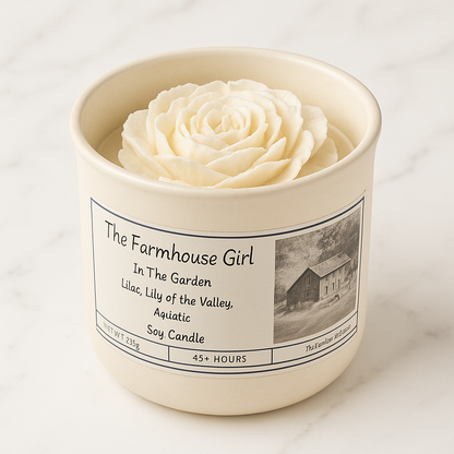 Candle with a rose inside labeled 'The Farmhouse Girl' on a white background
